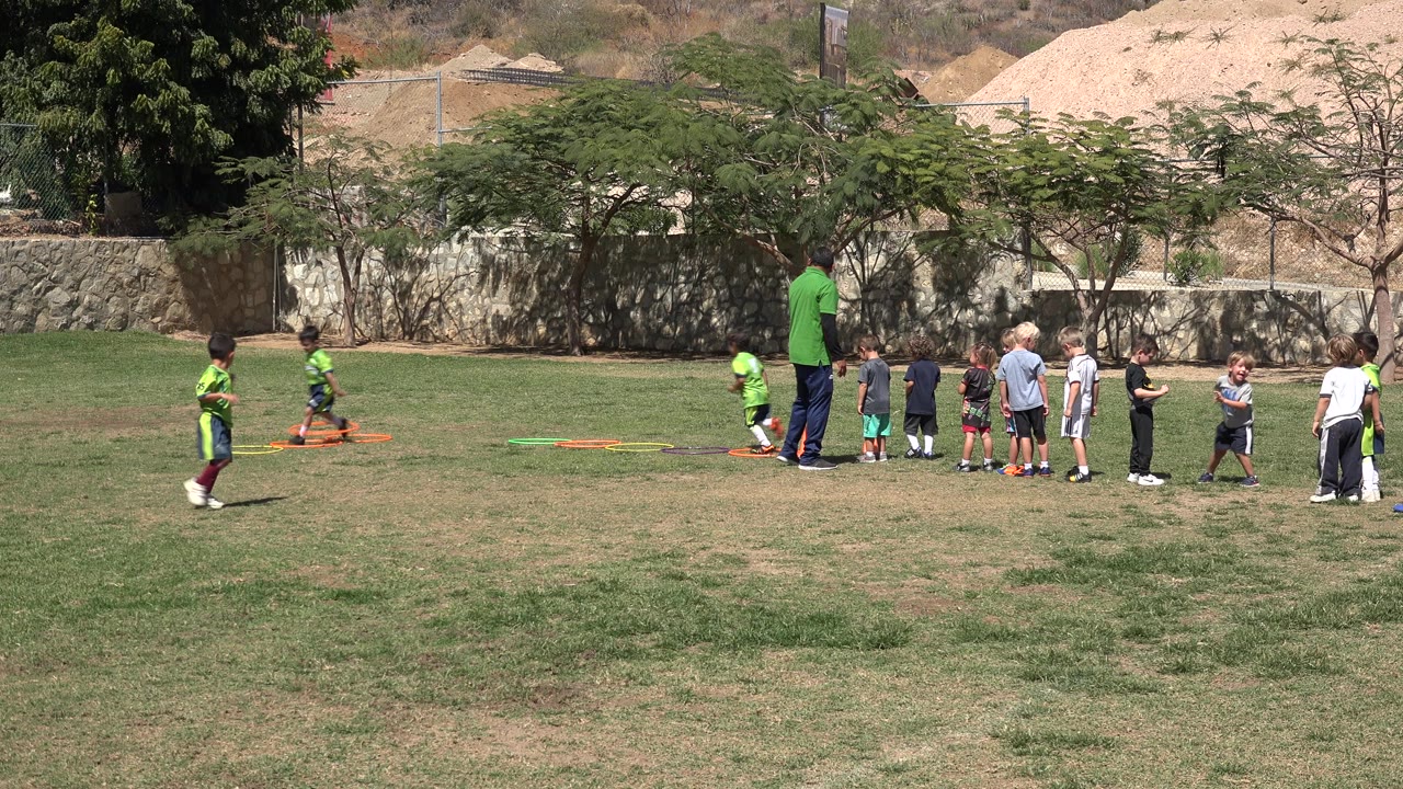 Coach and children on a grassy soccer practice field.
