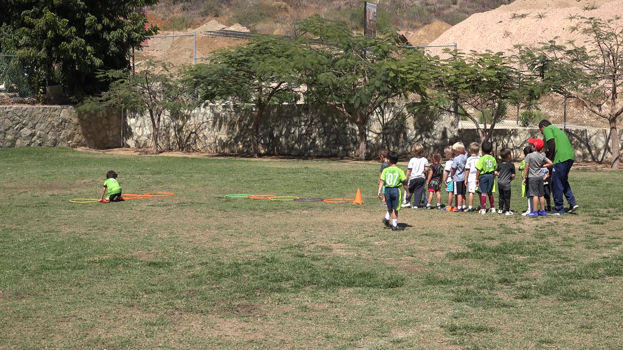 Boy in green shirt running on a soccer field near children and a coach.