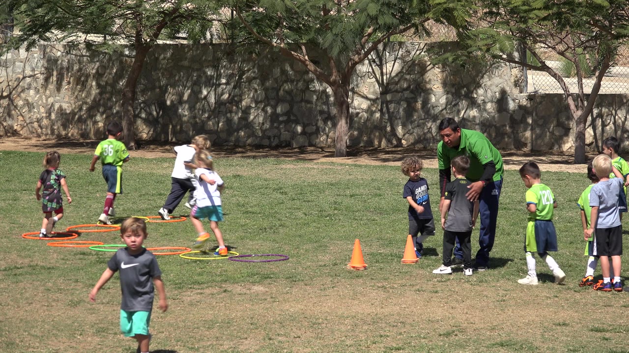 Children and a coach on a grass field with hoops and cones.