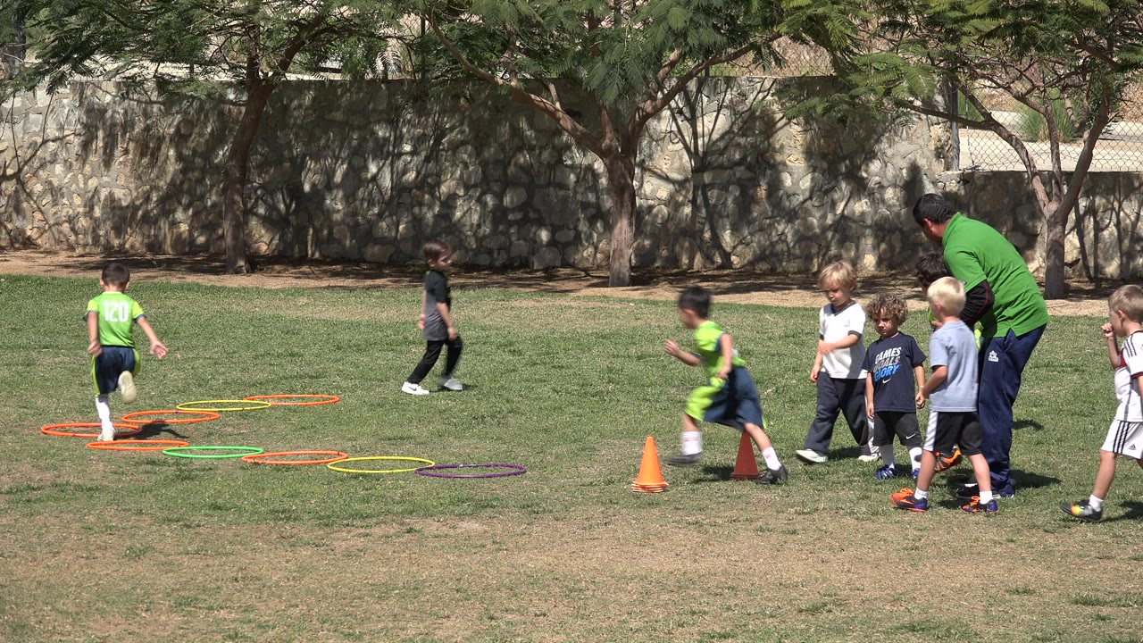 Children and a coach near agility rings on a grass field.