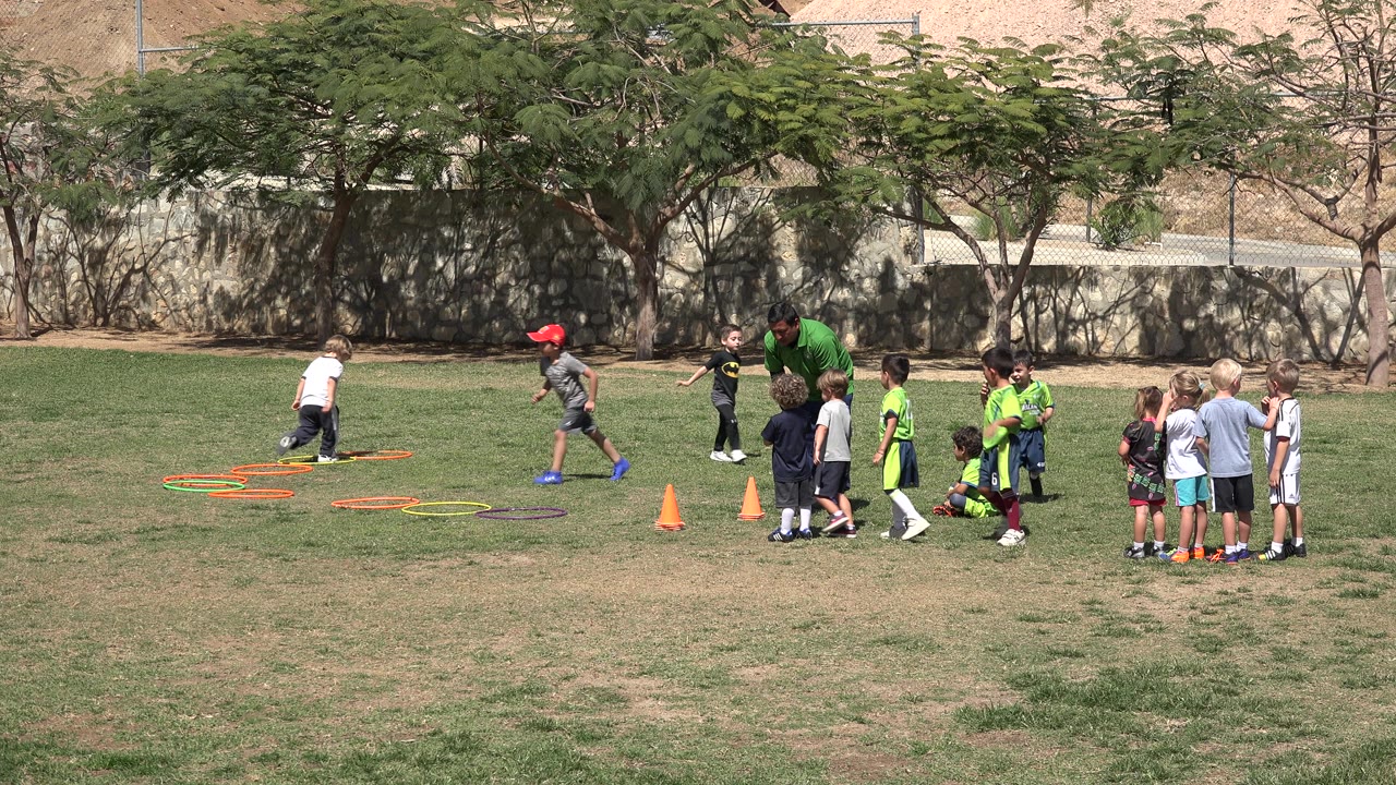 In San Jose del Cabo, Mexico, a child moves near the orange hoops as a small group of children waits to the right beside the adult in green.