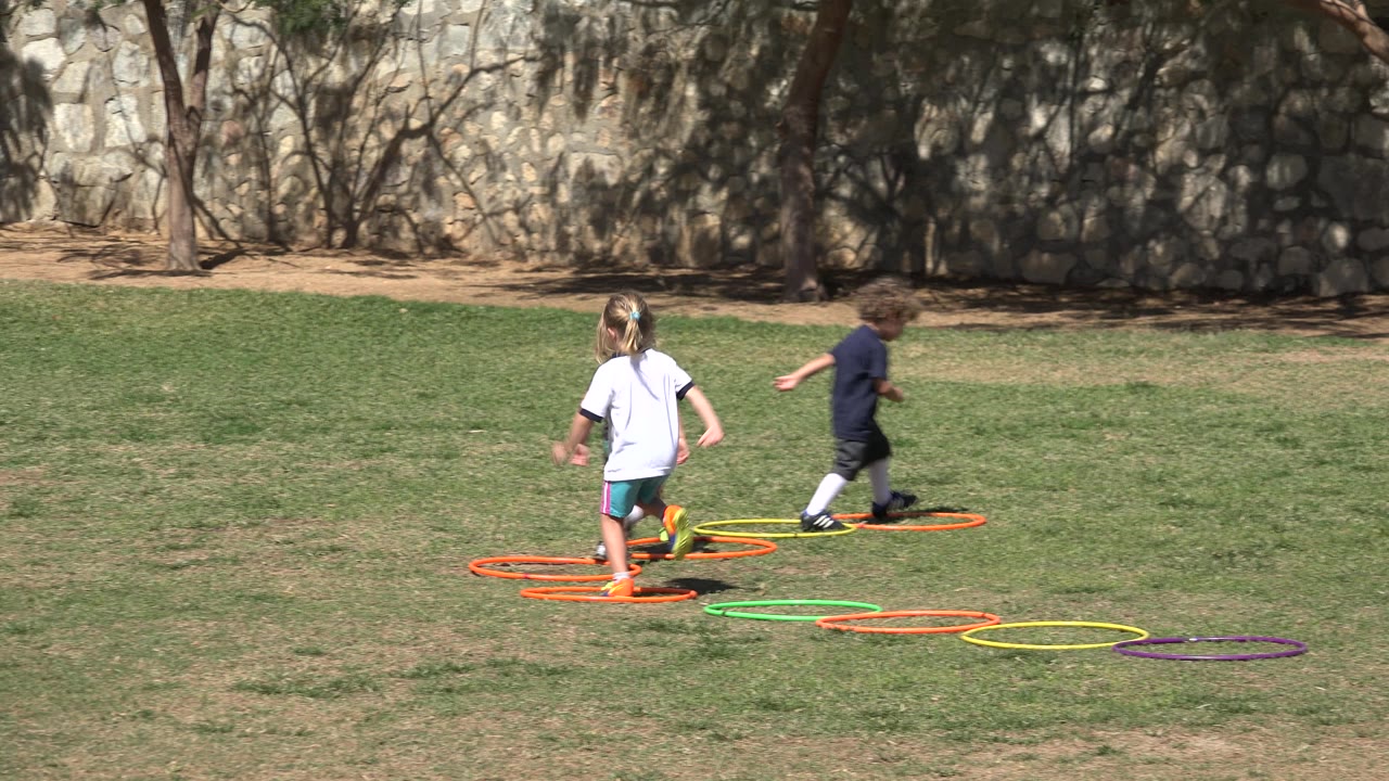 Two children run past hoops on a field.