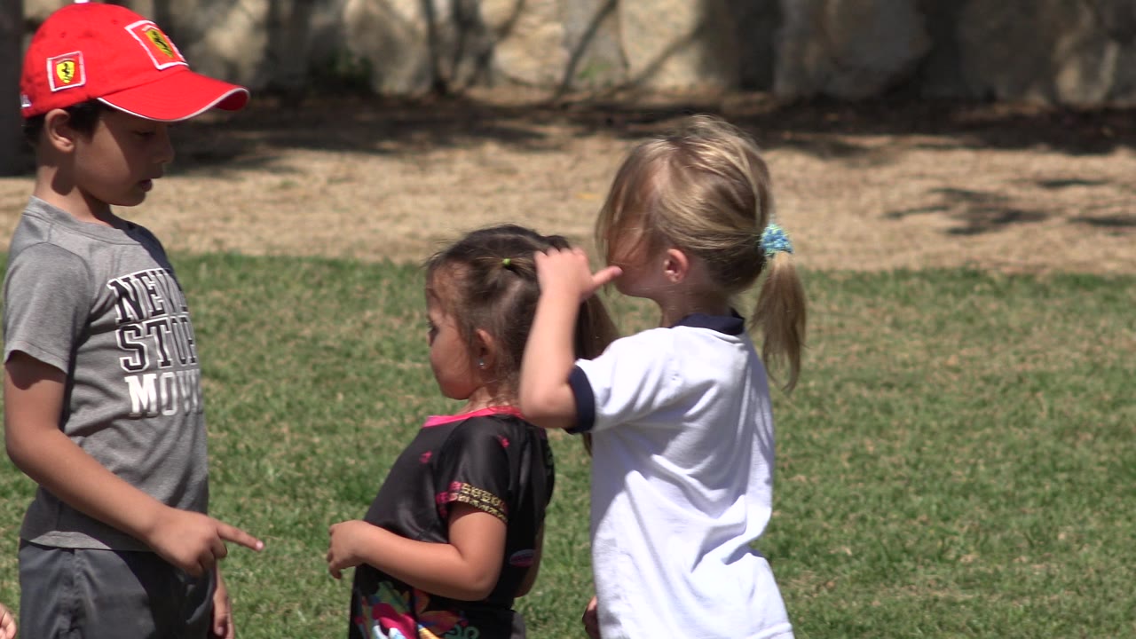Child in white shirt raises a hand beside two other children.