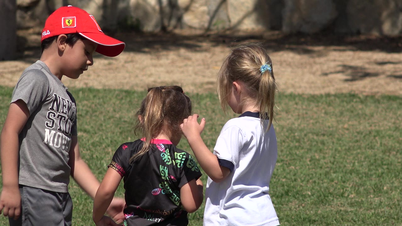 The boy in a red cap stands at the left while two girls face away or sideways on the grass field in San Jose del Cabo, Mexico.