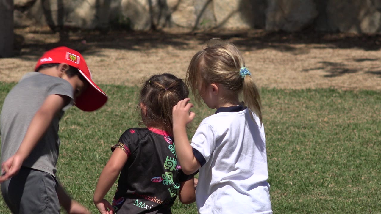 Boy in red cap and two girls playing on grass.