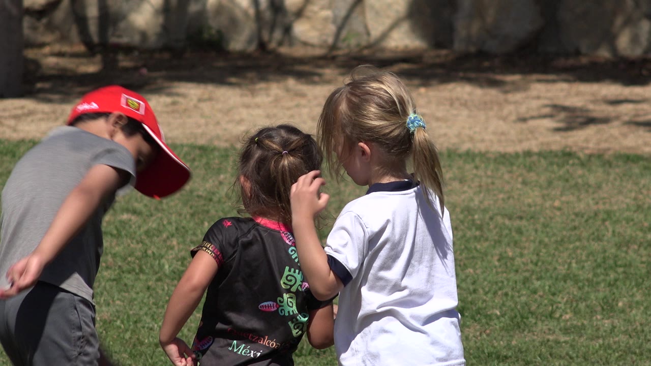 The boy bends forward near the two girls on the grass in San Jose del Cabo, Mexico, with the girls turned away from camera.