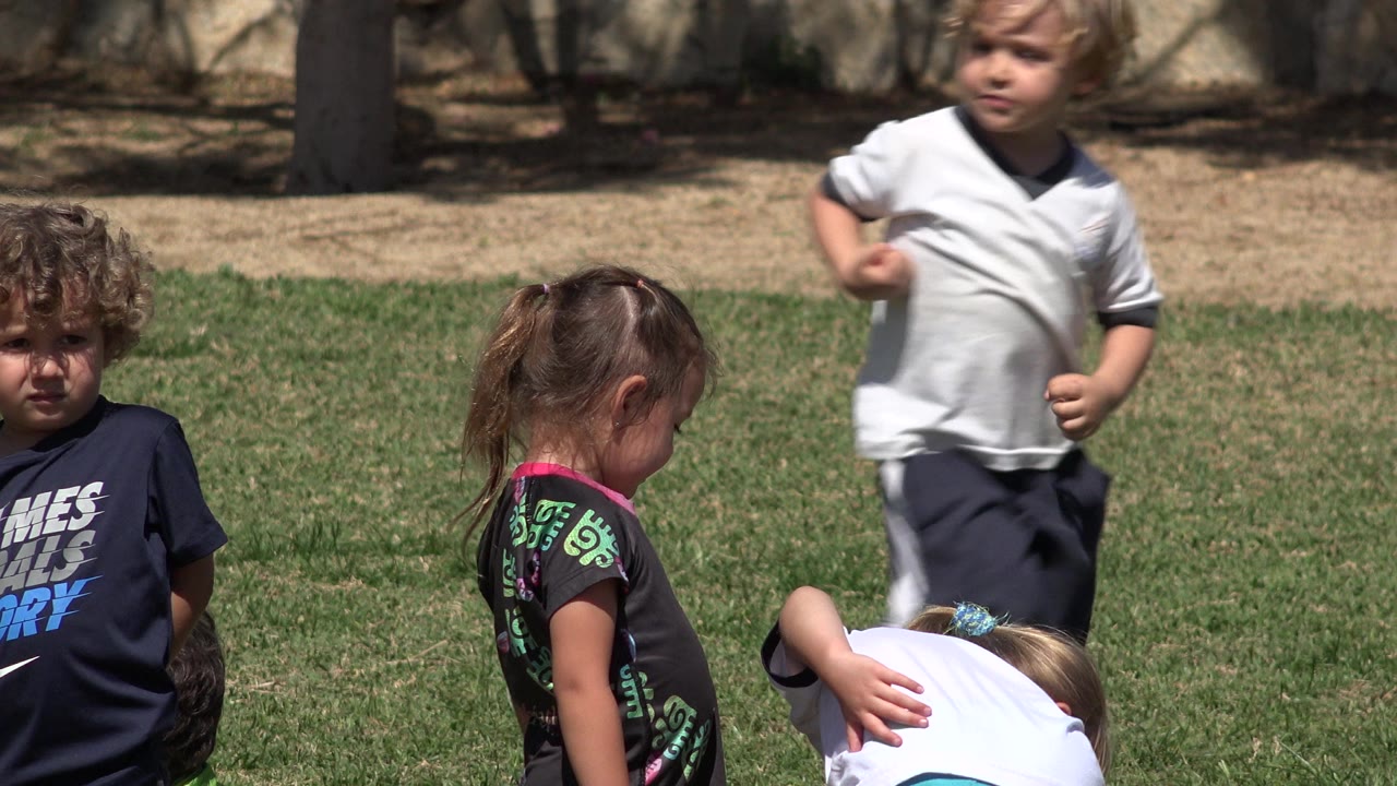 Children standing and bending on a sunny grass field.