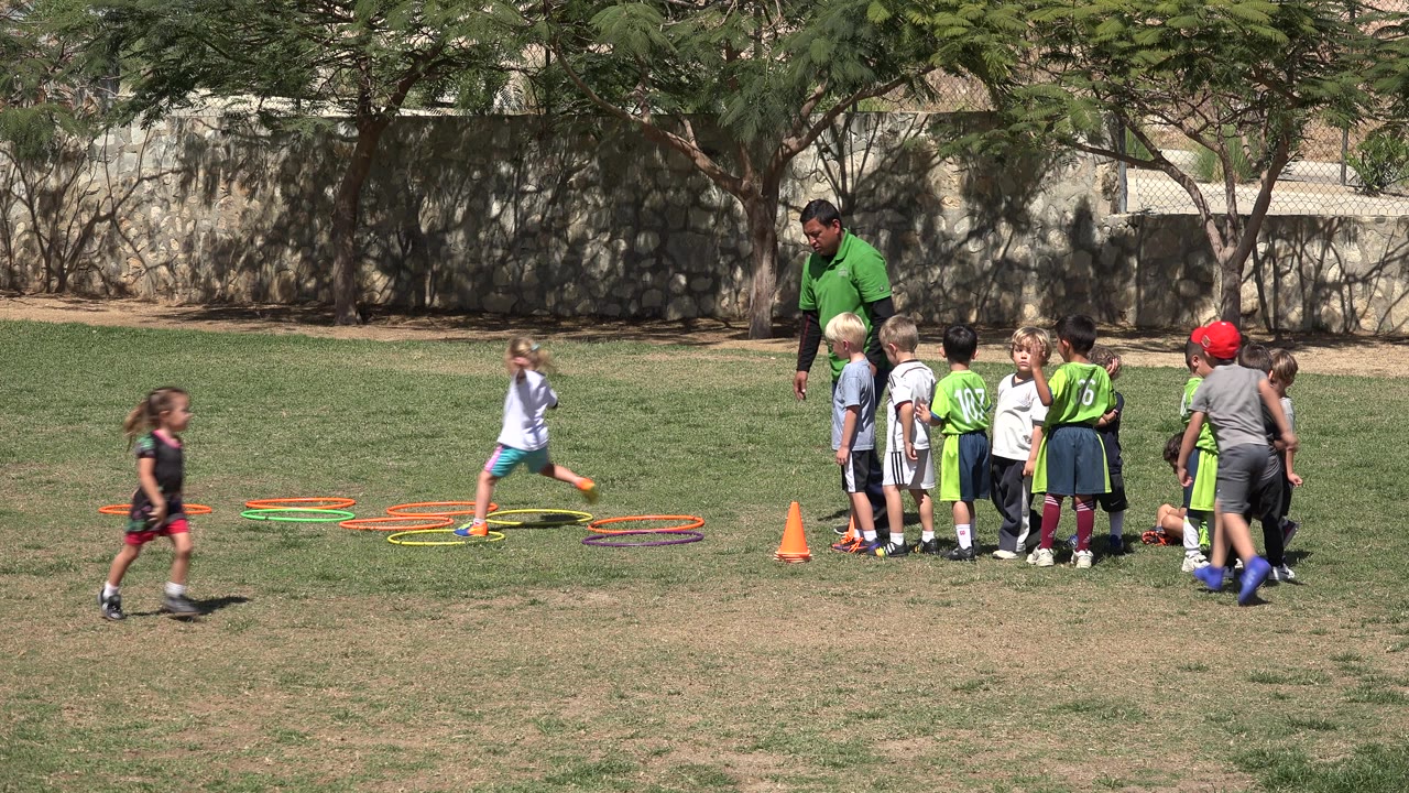 Children and a coach gather near soccer cones and hoops on a grass field.