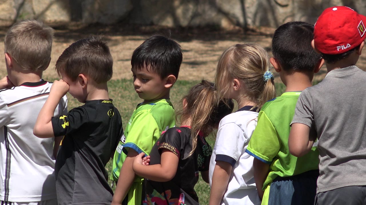 Children standing in a line on a sunny grass field.