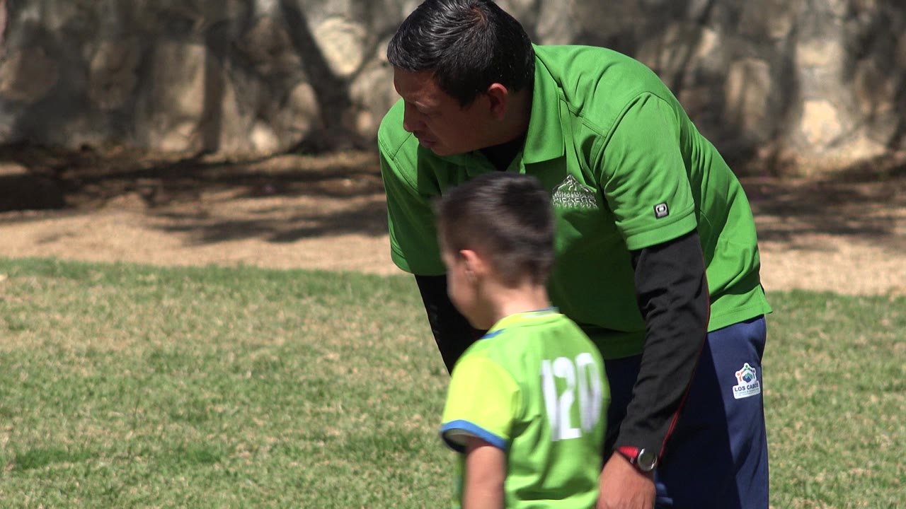 Trainer bends toward a child in a green jersey on the field.
