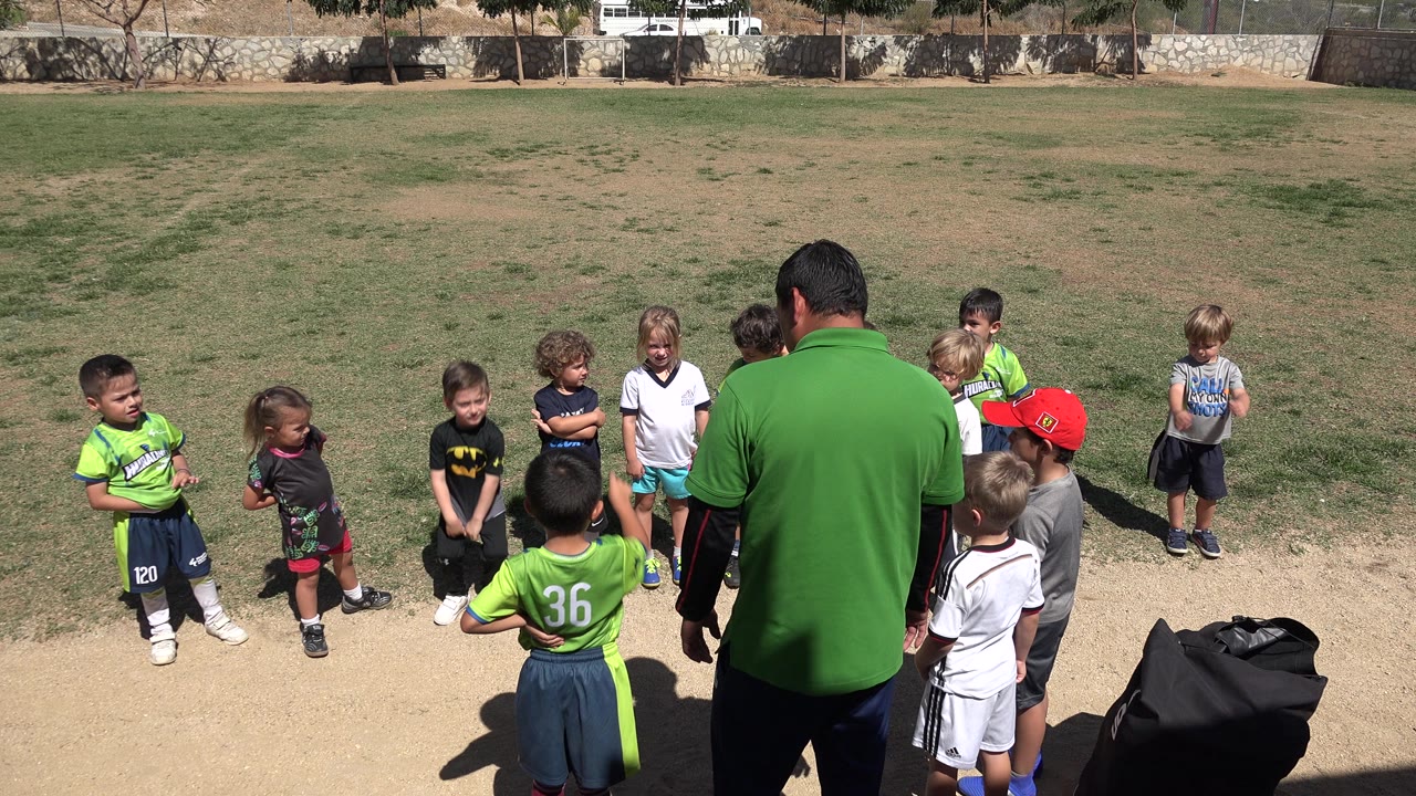 Children stand around an adult on a sunny grass field.