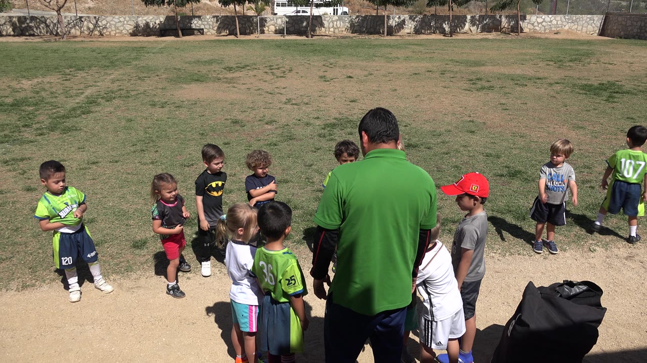 Children gather around an adult on a sunny grass field.