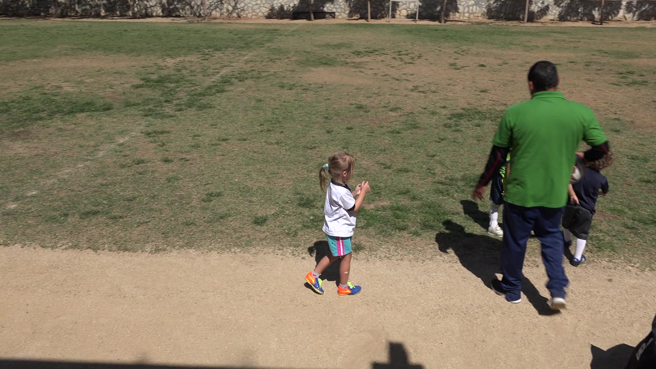 In San Jose del Cabo, Mexico, the adult continues along the field edge while a child in a white shirt follows near the dirt path and two children move ahead on the grass.