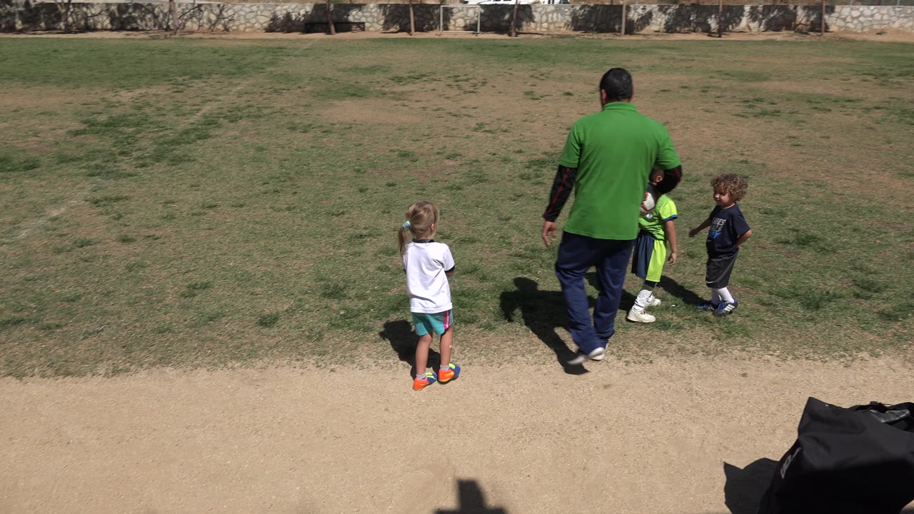 Adult and children walking away across a patchy grass field.