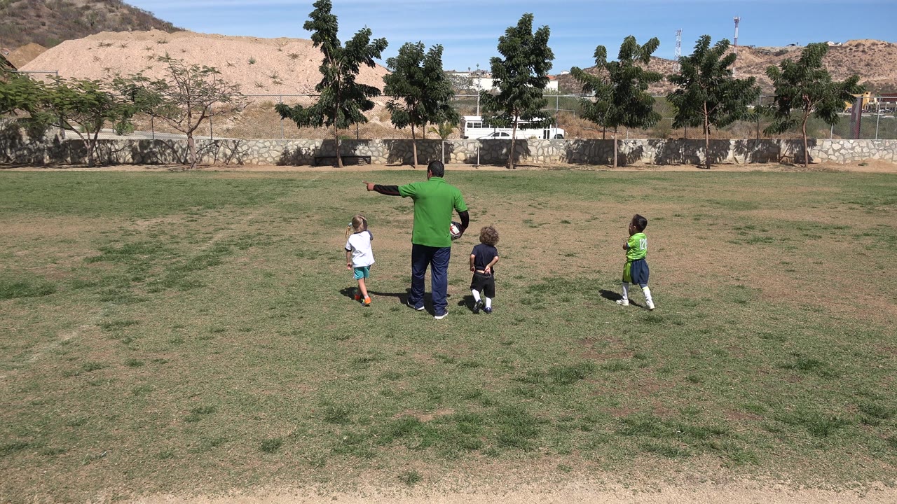 Adult pointing while children stand nearby on grass.