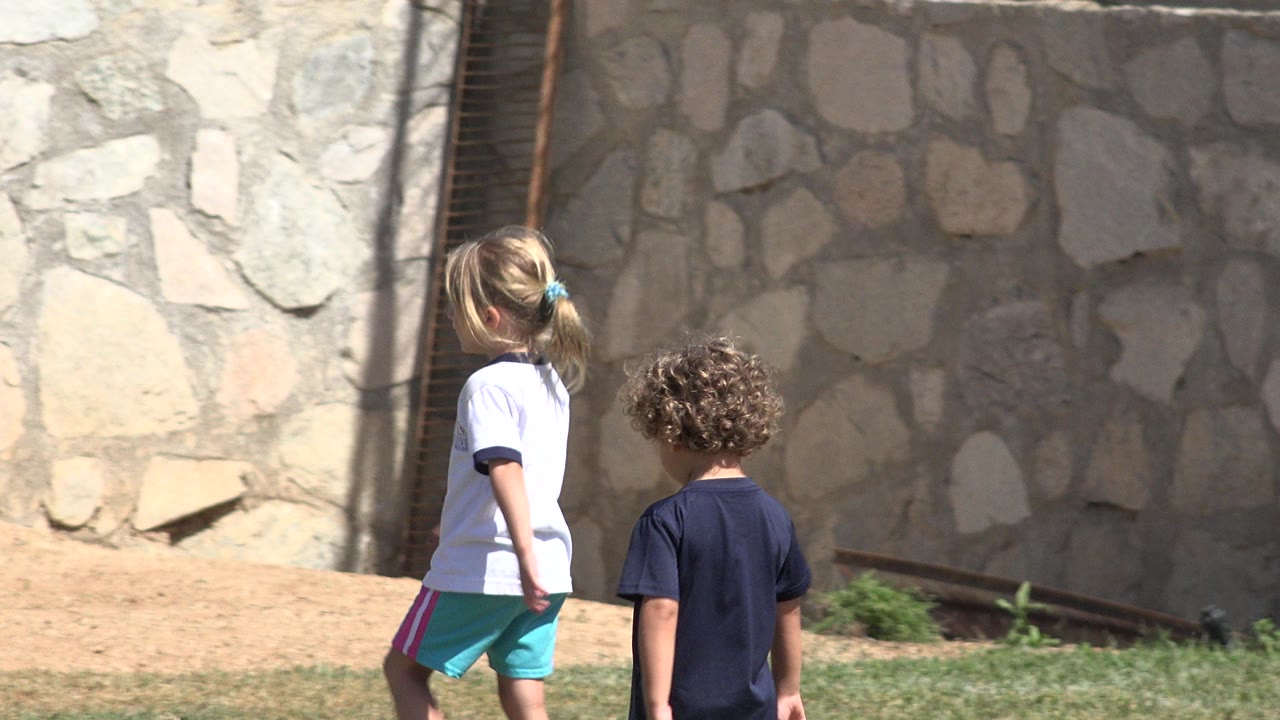 Two children walking beside a stone wall on a soccer field.