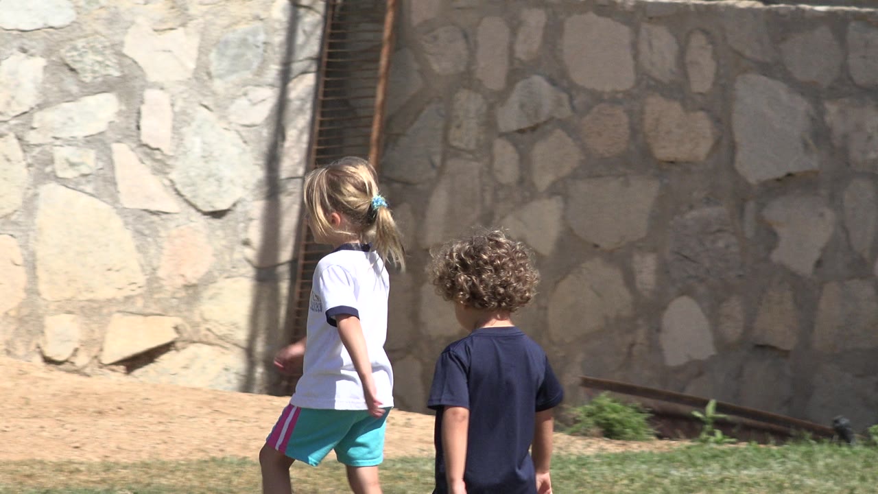 The same two children continue across the field in San Jose del Cabo, Mexico, with the child in white slightly ahead and the stone wall filling the background.