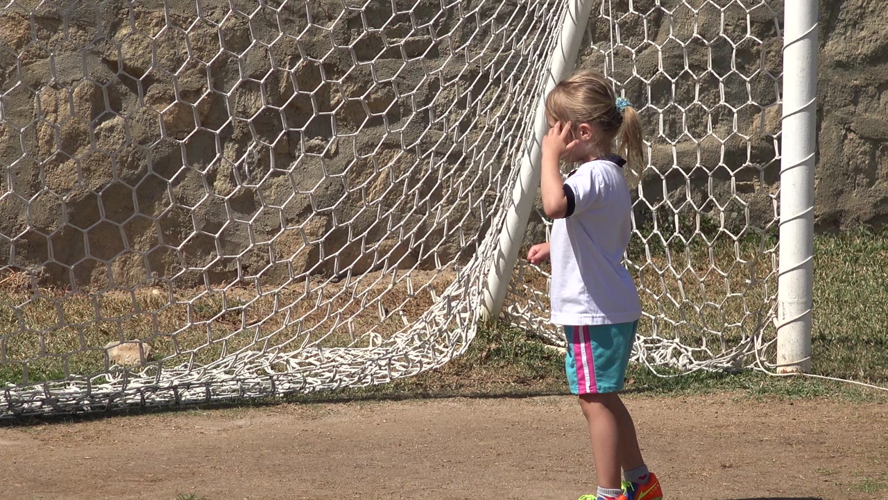 Young girl standing beside a soccer goal net.