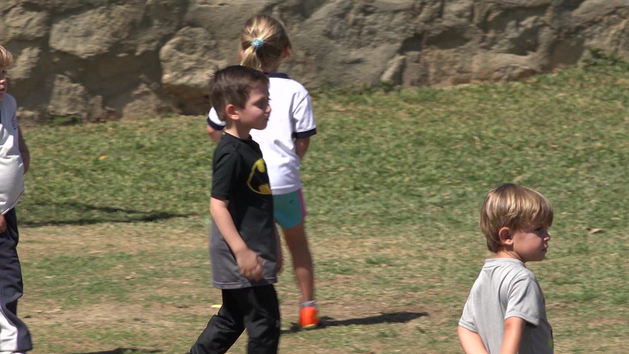 A boy in a dark shirt and other children in light shirts stand and move across the grass field in San Jose del Cabo, Mexico.
