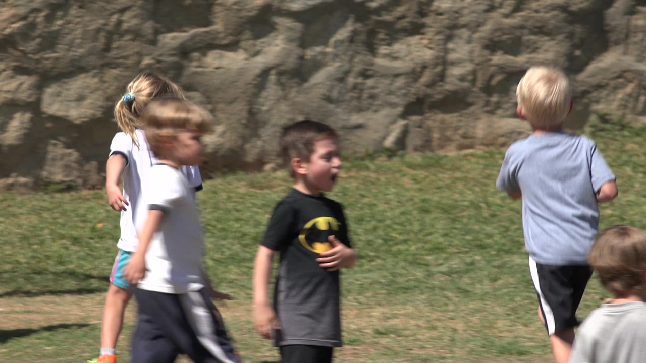 Children walking near the field as play shifts toward the goal.