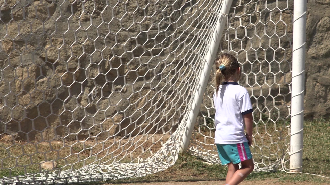 Young girl standing near a white soccer goal net on a grass field.