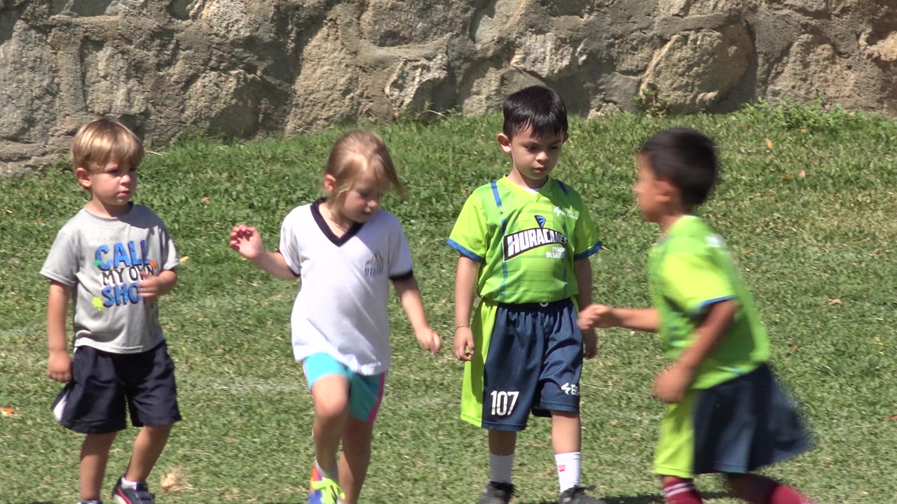Four children on grass, including one child blurred while running past.
