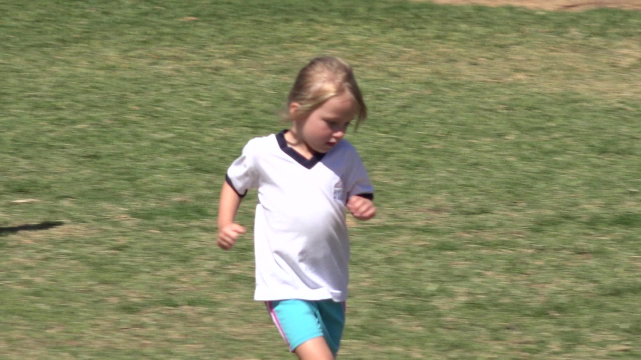 Young girl in a white athletic shirt runs across a grass field in San Jose Del Cabo, Mexico, with the field filling the background.