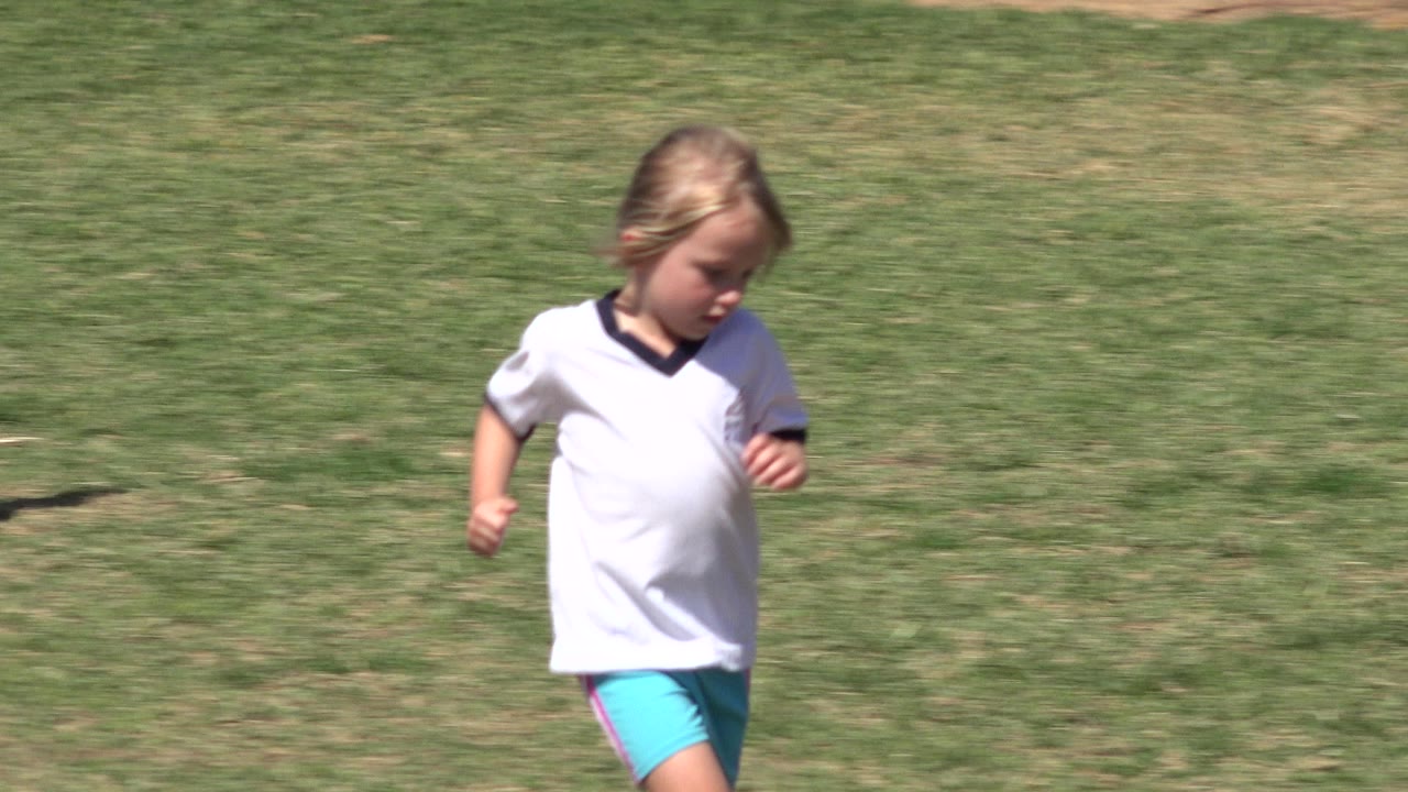 Young girl continues across the grass field in San Jose Del Cabo, Mexico, her head angled down as bright sun casts sharp field shadows.