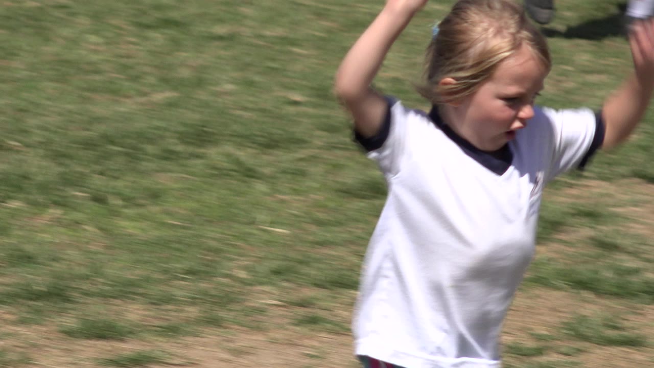 Blonde child in white soccer shirt running on grass field