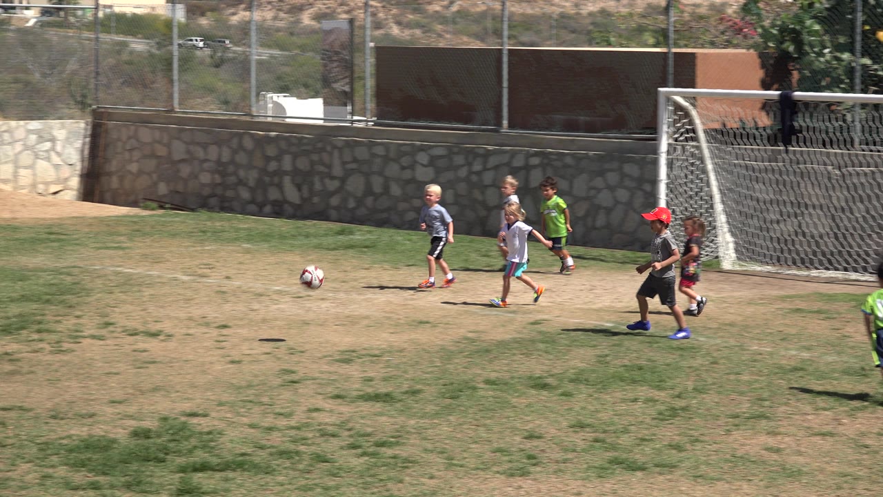 Children run near a soccer goal on a dry grass field.