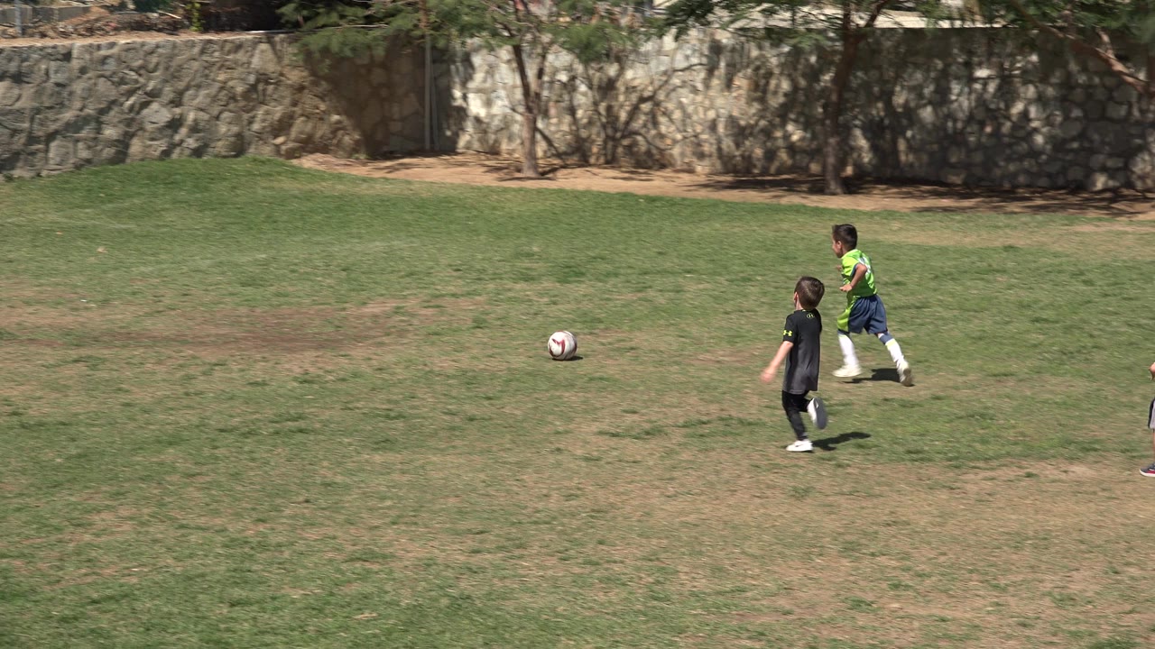 Two children run toward a soccer ball on a grass field.
