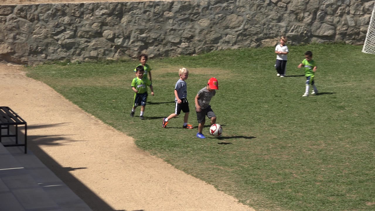 A child in a red cap runs with a soccer ball.