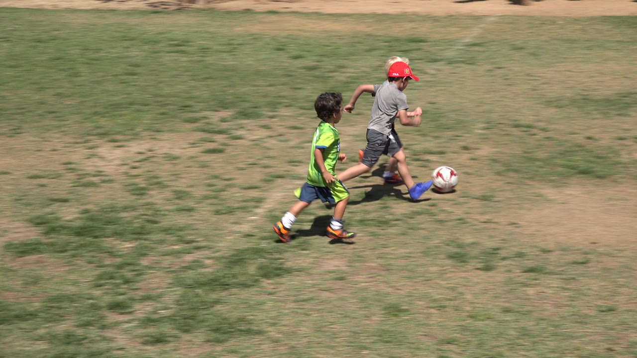 Children run in a line behind a soccer ball.