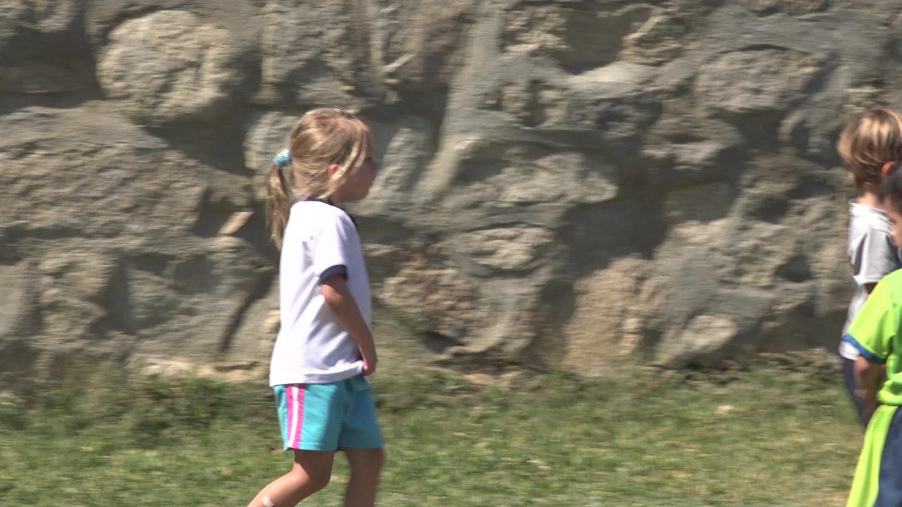 A child in a gray shirt and dark shorts walks away from camera along the grassy field with a stone wall behind in San Jose Del Cabo, Mexico.