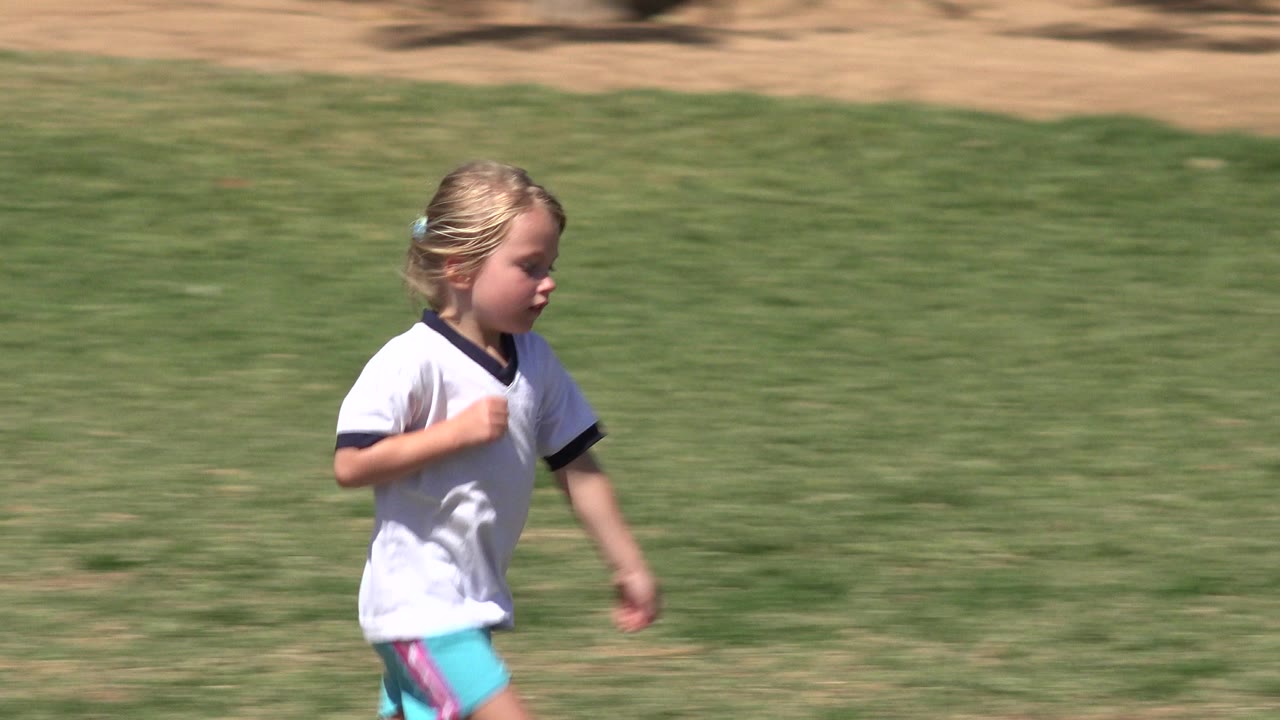 Young girl running on grass in a white shirt.