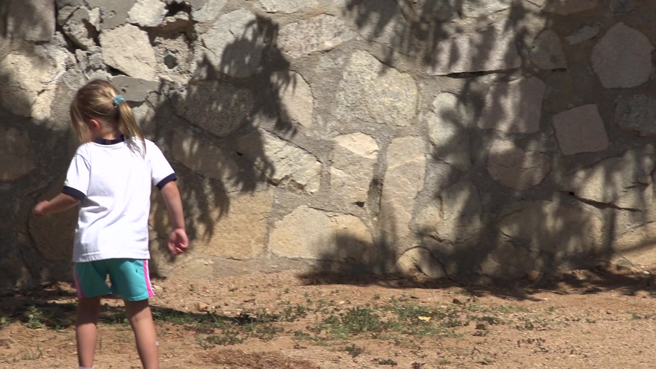 Girl standing near a stone wall in bright sun.
