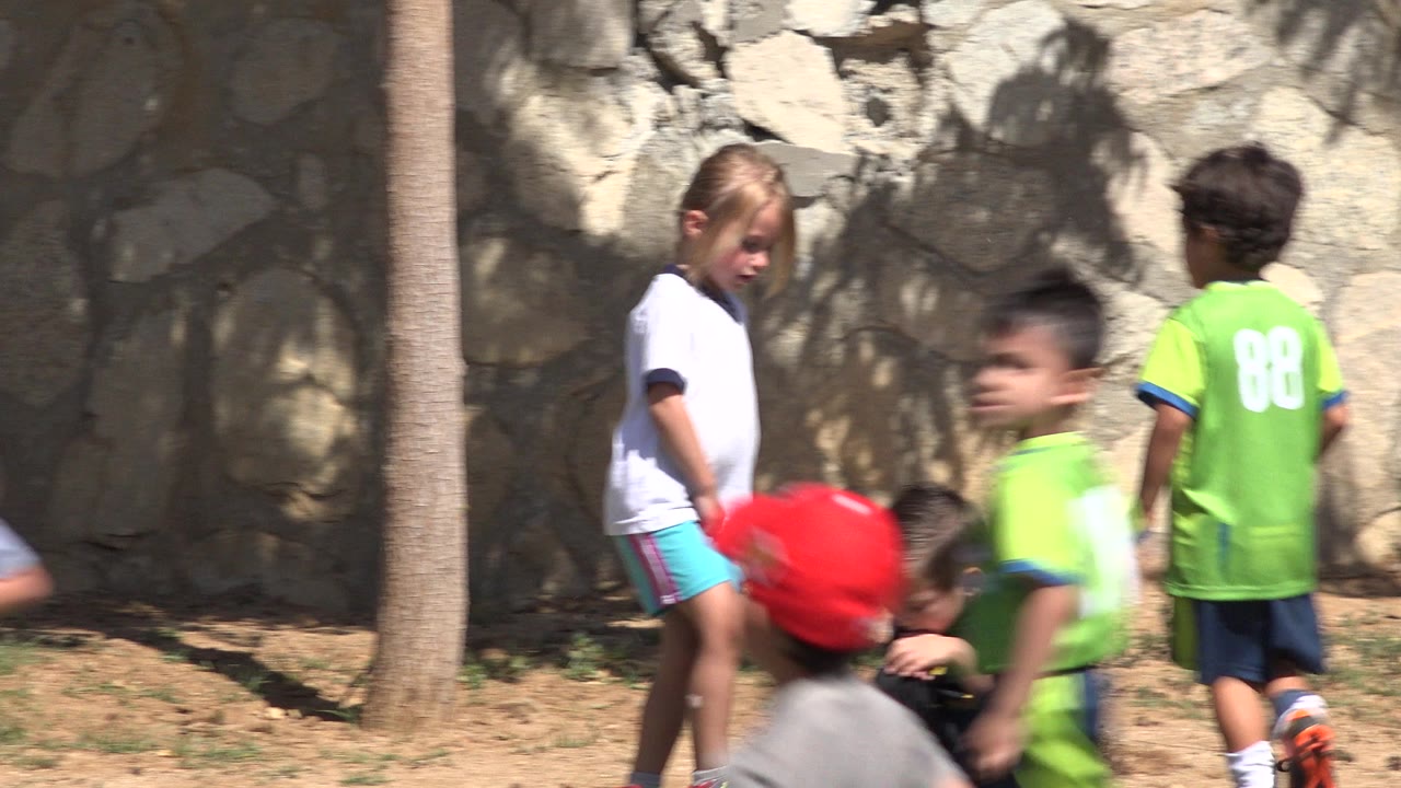 Children near a stone wall as a blonde girl stands by the grass.