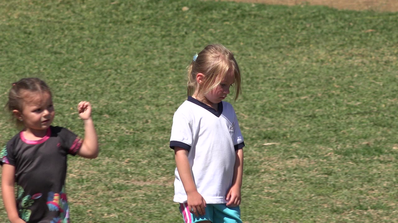 Two young children walking on a grass field in bright sun.
