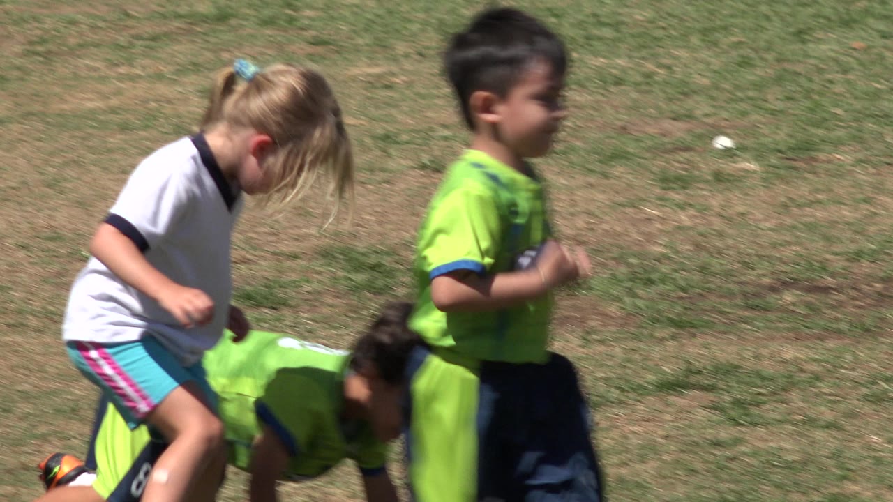 Children in soccer clothes running on a patchy grass field.
