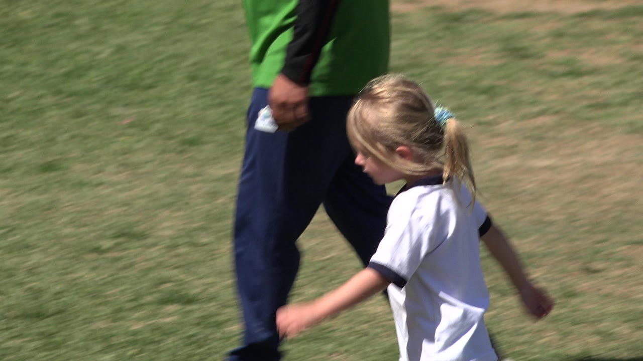 Girl walking near an adult on a sunny grass field.