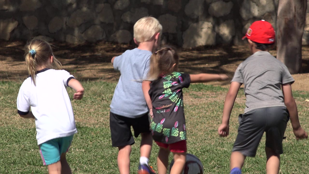 At 0:01, three children remain centered from behind while running across the sunlit field in San Jose Del Cabo, Mexico, with another child partly visible at the left edge.