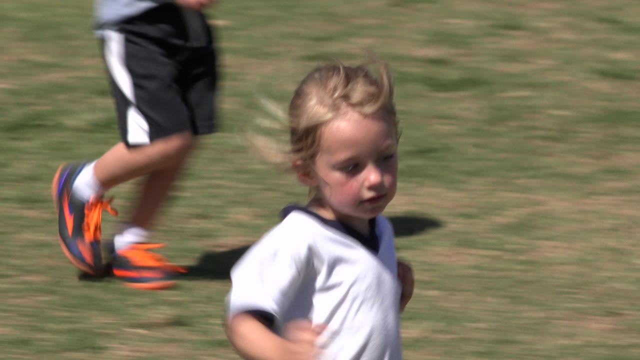 Girl running near the right side of the frame with children's legs crossing behind her.