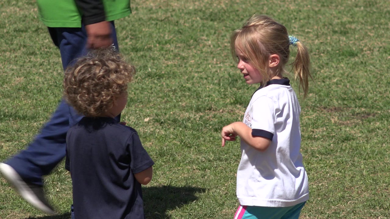 Two children on grass with adult legs entering the frame.