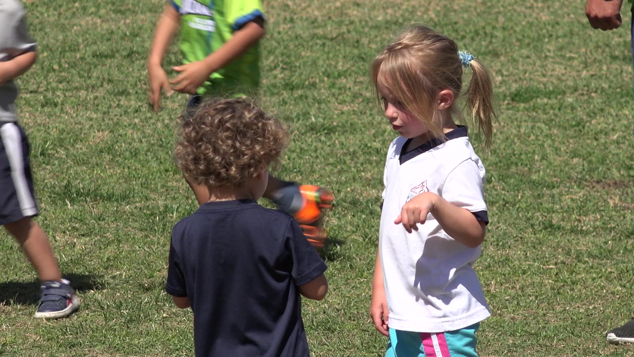 Young girl in a white shirt faces a curly-haired child on a grassy field.