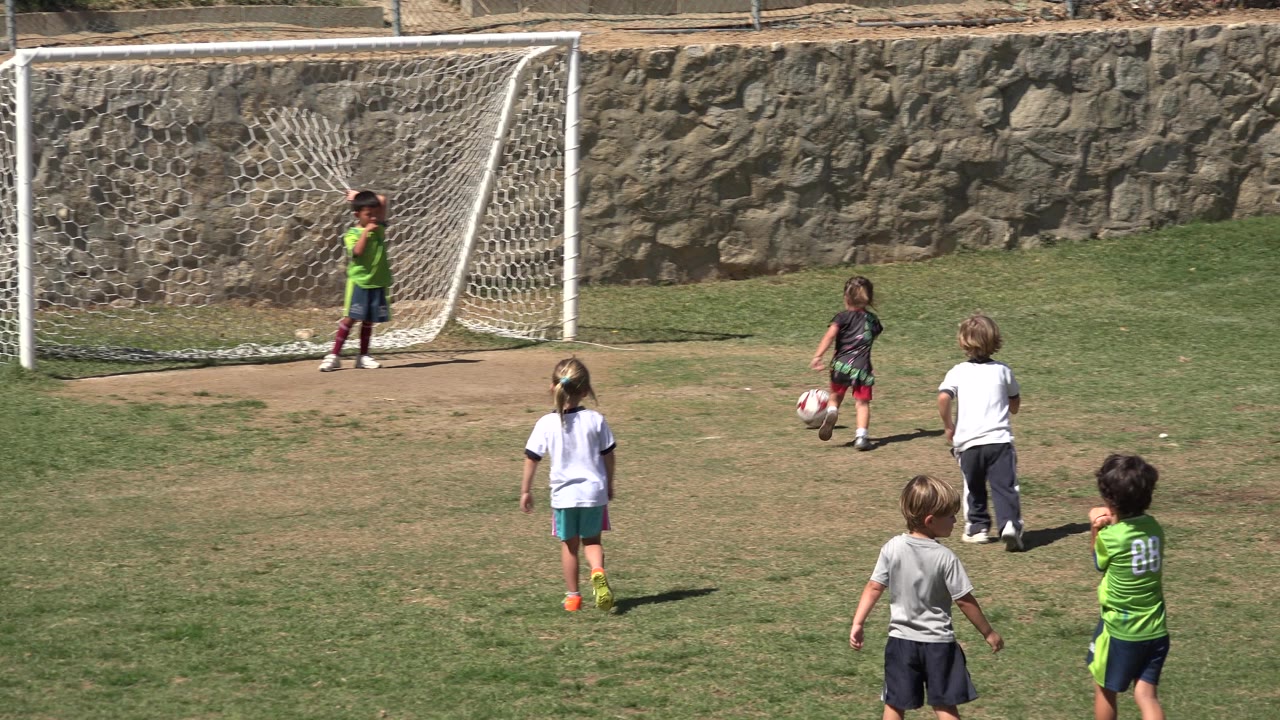 A young girl stands with the soccer ball in front of the white goal in San Jose del Cabo, Mexico, while the child goalkeeper waits inside the net and other children look on.