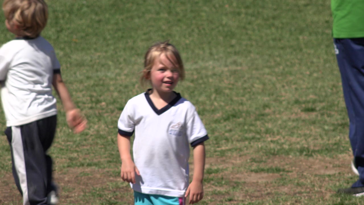 Young girl on grass field with boy and adult partly visible