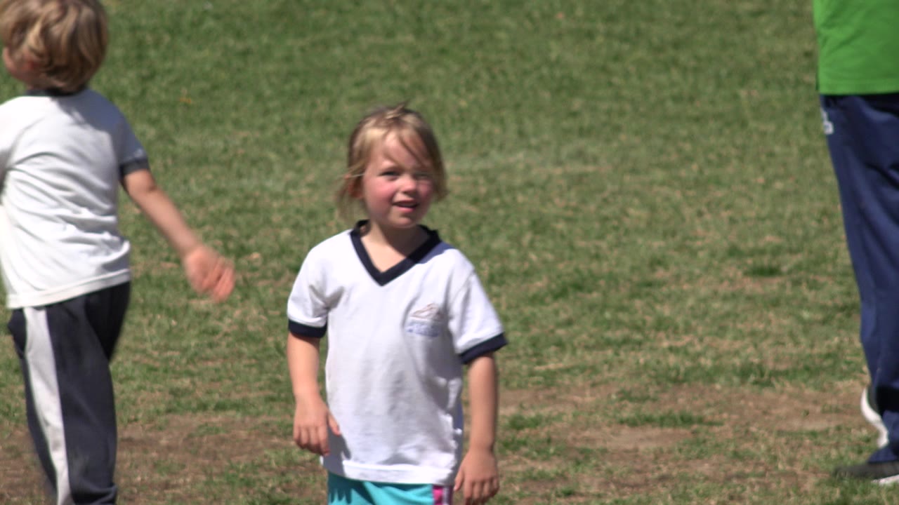 The girl remains near the center of the San Jose del Cabo grass field while a boy and a partially visible adult move behind and beside her.