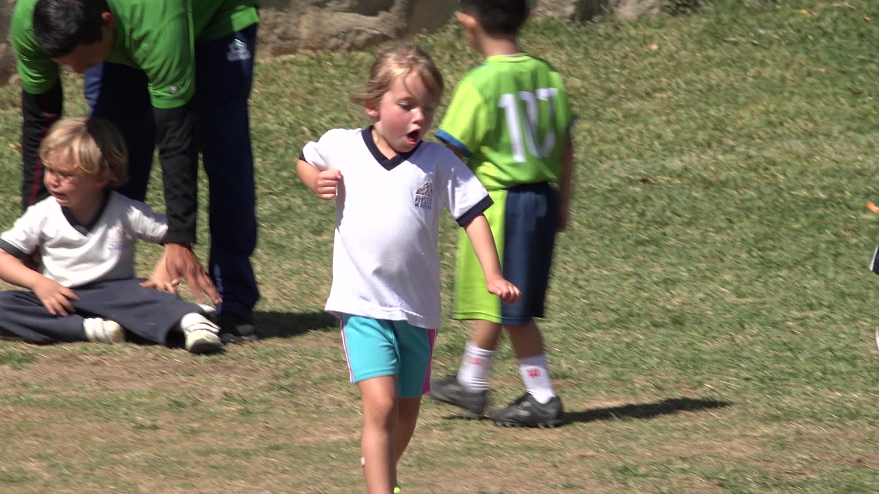Children on a grassy field with a blond child walking in front.