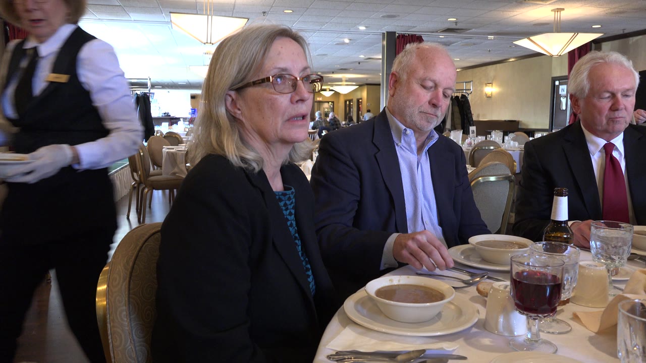 Three adults sit at a Chicago restaurant table with soup bowls, glassware, beer bottles, and place settings, while the dining room and bar area remain visible behind them.