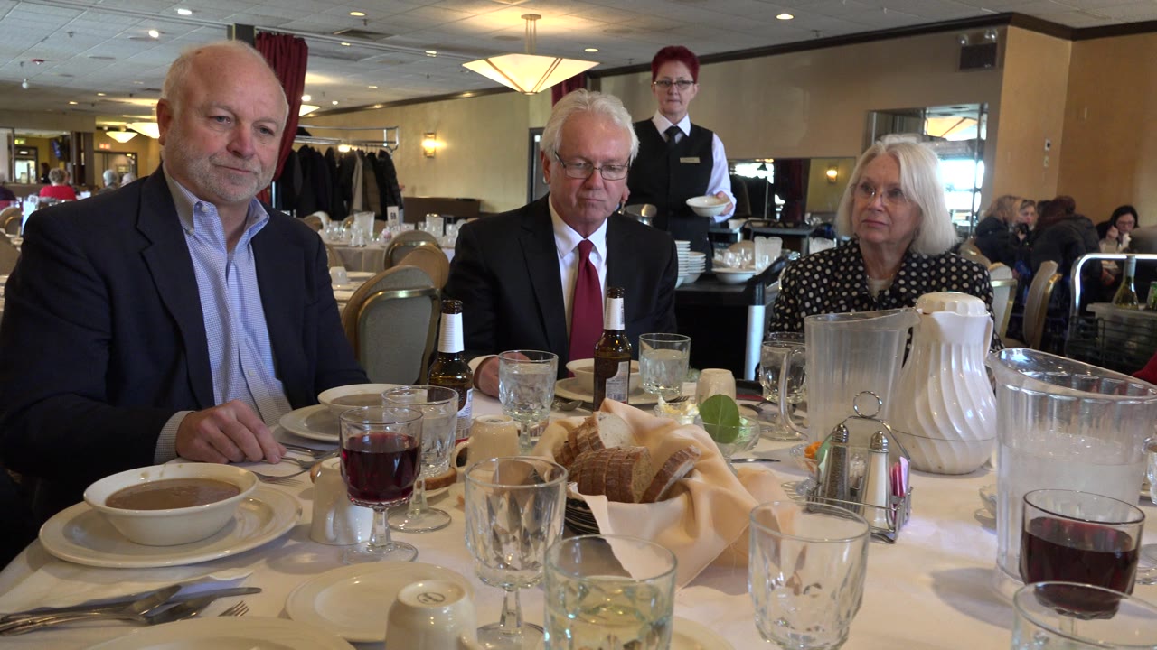 Adults seated at a restaurant table with soup, drinks, bread, and a server behind them.